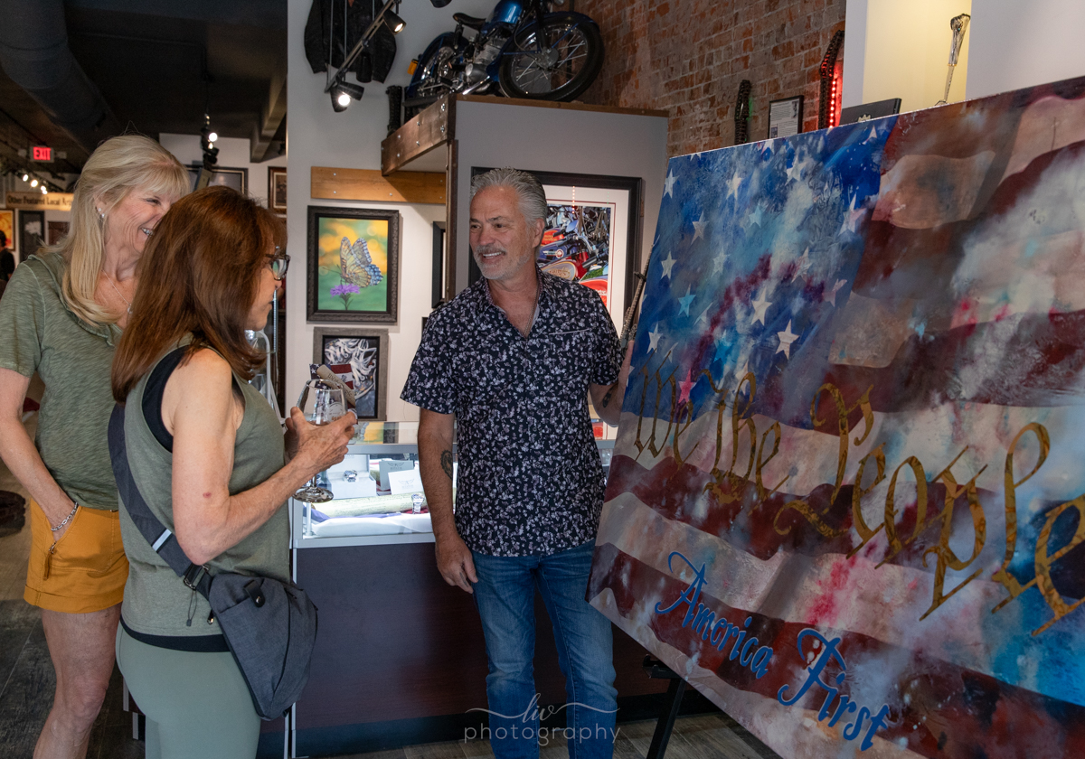 Scott Jacobs showing the completed patriotic painting, America first to two women in Jacobs Gallery Deadwood